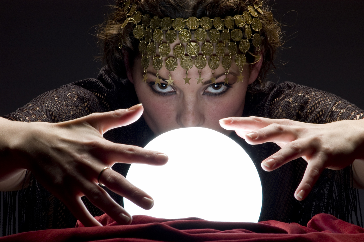 Close up of mysterious focused fortune telling woman wearing a copper hair dress with her hands on a glowing crystal ball looking at the camera